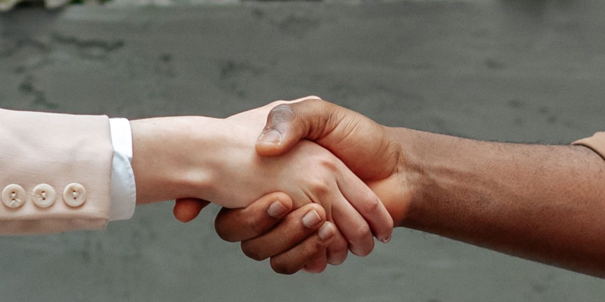 Two business professionals shaking hands over a table, symbolizing the start of a new, promising partnership and onboarding phase.